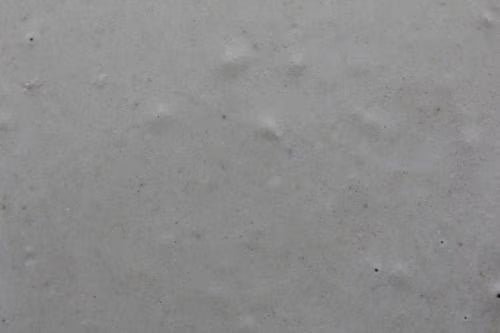 A close-up of a light gray textured surface with subtle pitting and speckling.