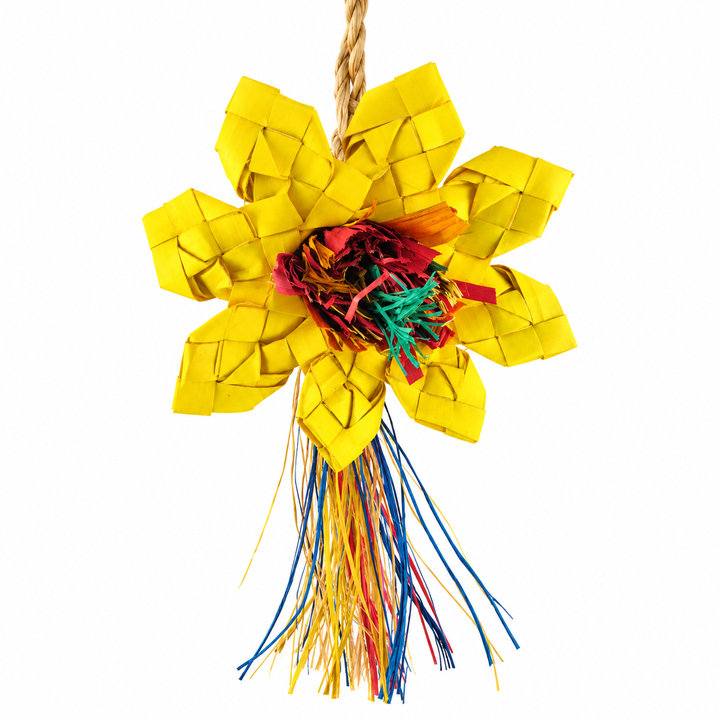 A woven pet toy shaped like a flower, featuring bright yellow woven petals, a colorful fringed center in red, orange, and green, and a long hanging tail with multicolored strands, suspended from a rope on a white background- Planet Pleasures Sunflower Bird Toy – Small